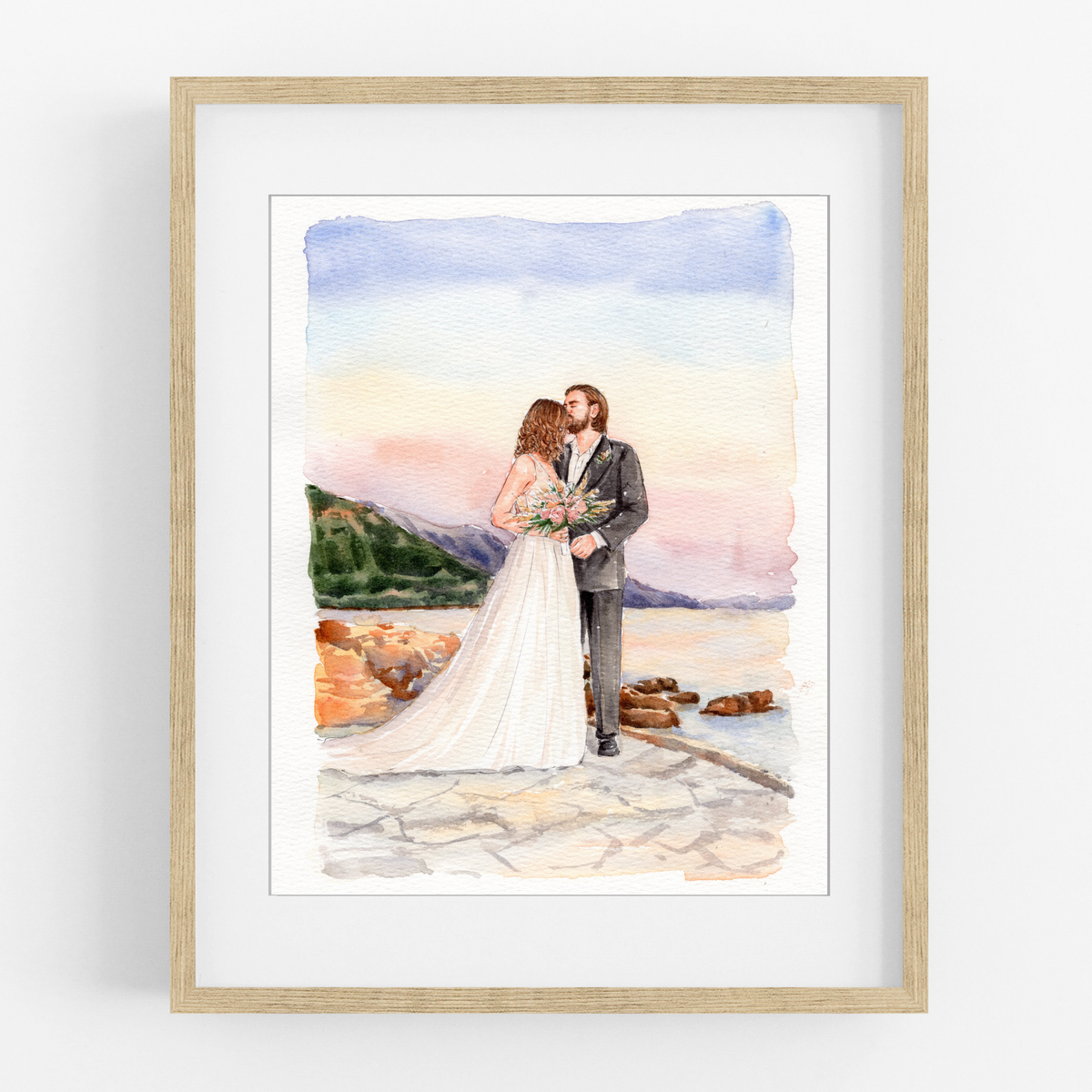 Framed watercolor portrait of a bride and groom embracing on a beach beside rocks and blue water.