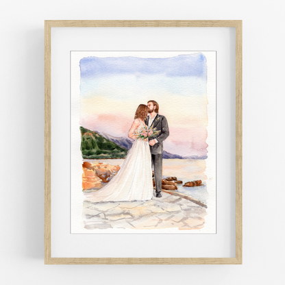 Framed watercolor portrait of a bride and groom embracing on a beach beside rocks and blue water.