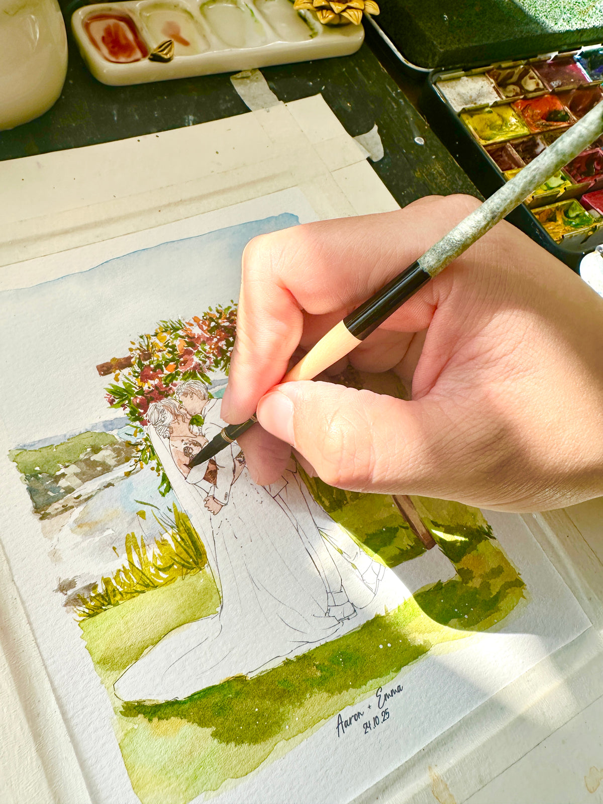 Close-up of an artist hand-painting a bride's dress in a watercolor garden wedding portrait.