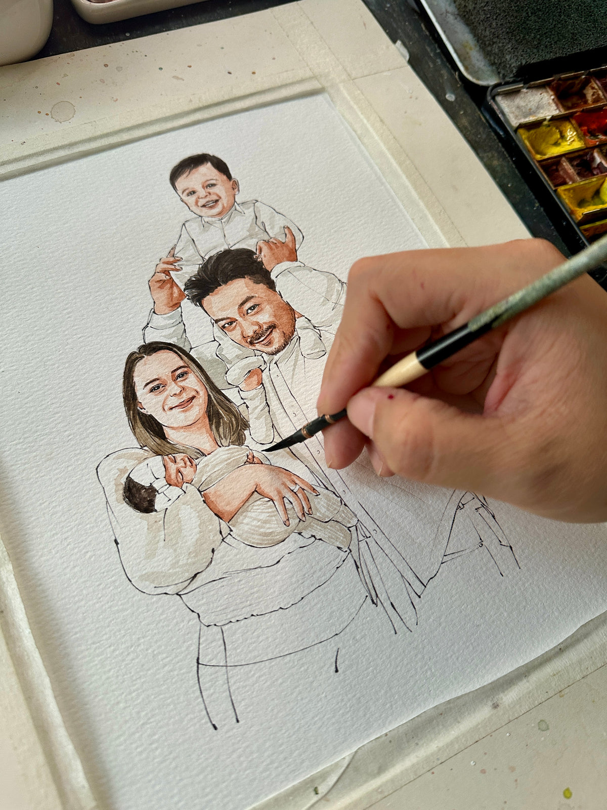 Close-up of an artist painting a family watercolor portrait with parents, a baby and a child on the father's shoulders.