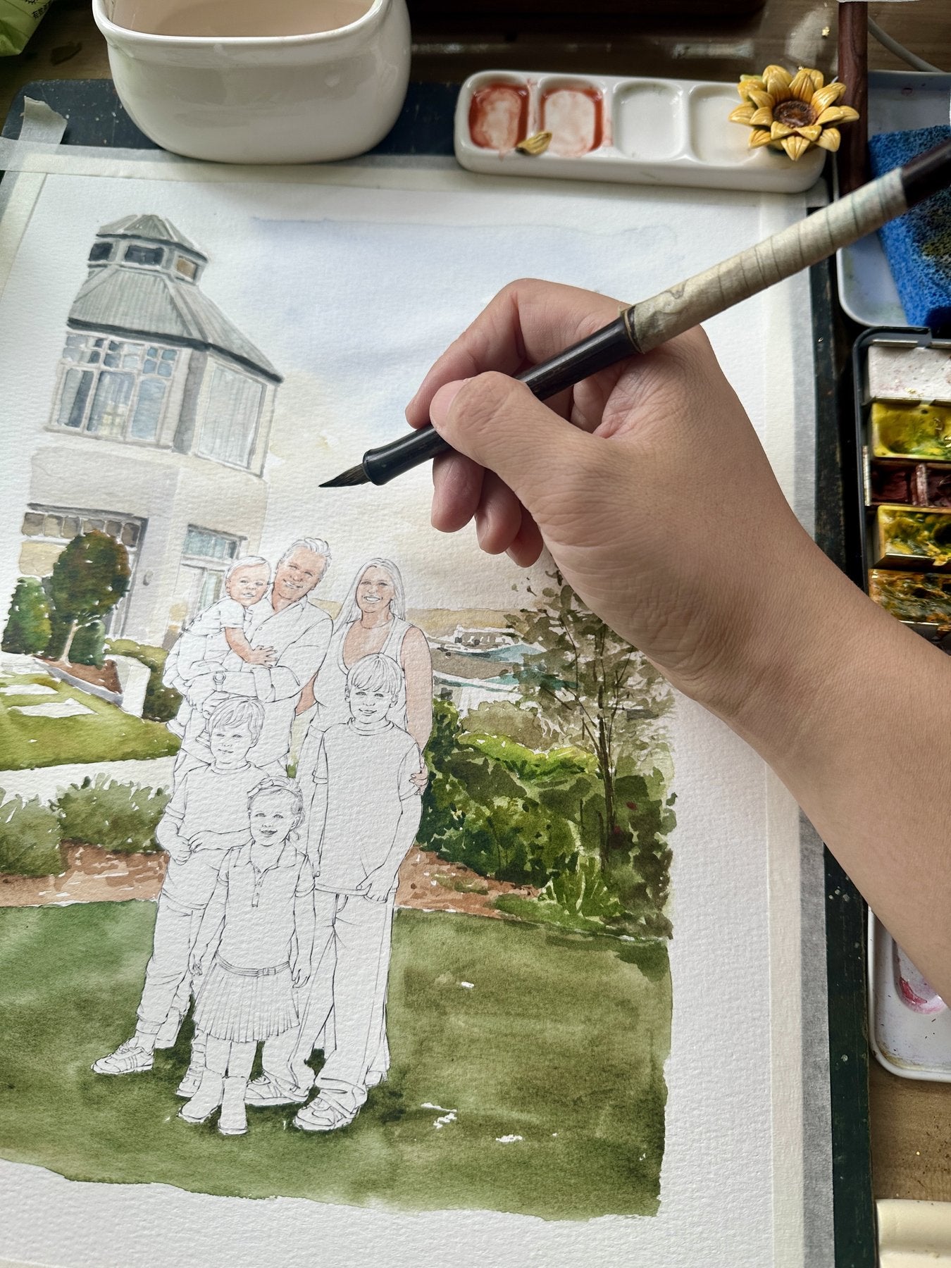 A large family watercolor portrait being painted in front of their home