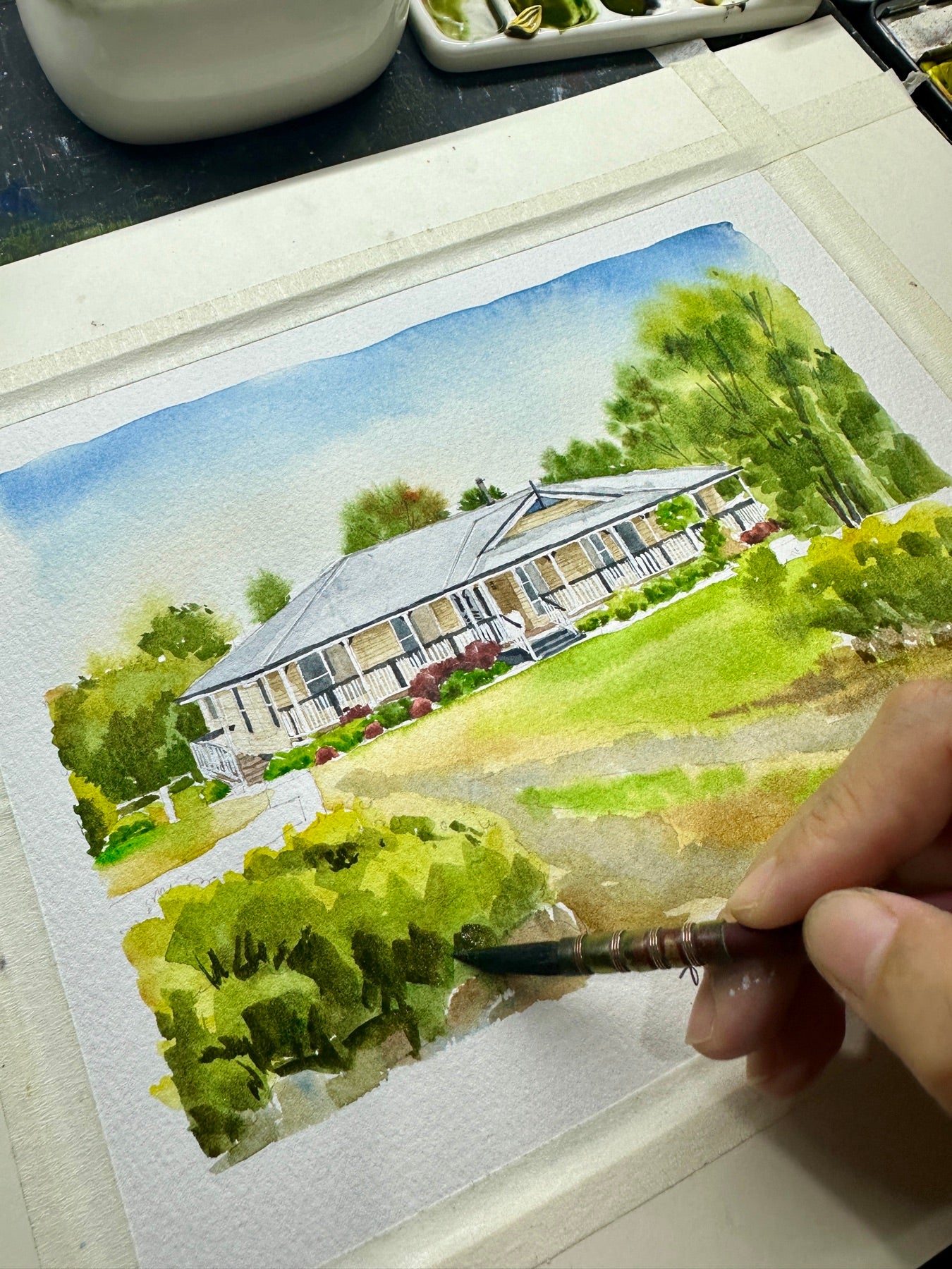 Artist hand-painting a watercolor portrait of a country home with a long veranda