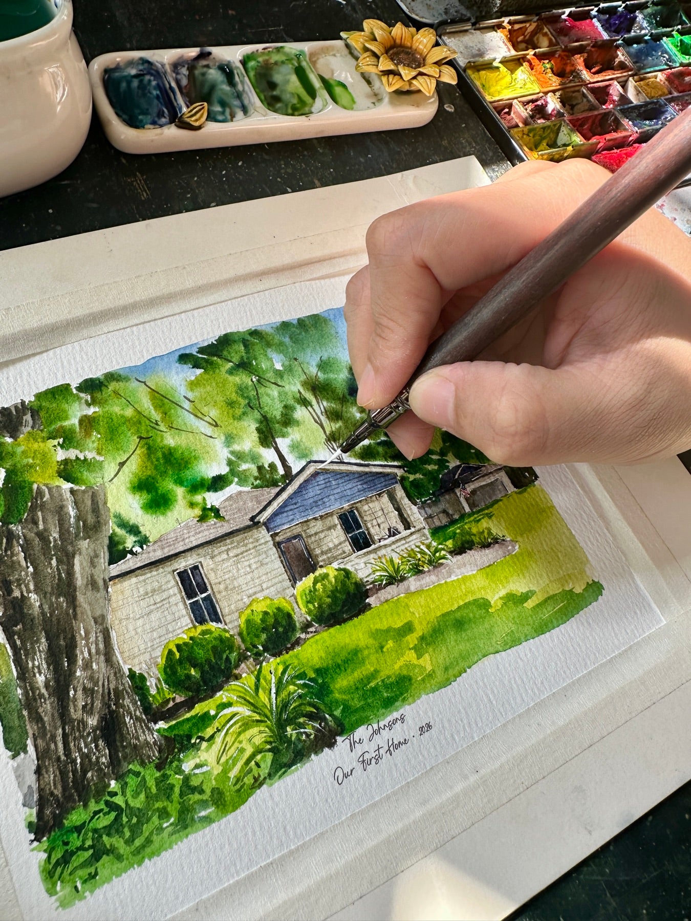 Artist hand-painting a watercolor portrait of a single-story home with a blue gable