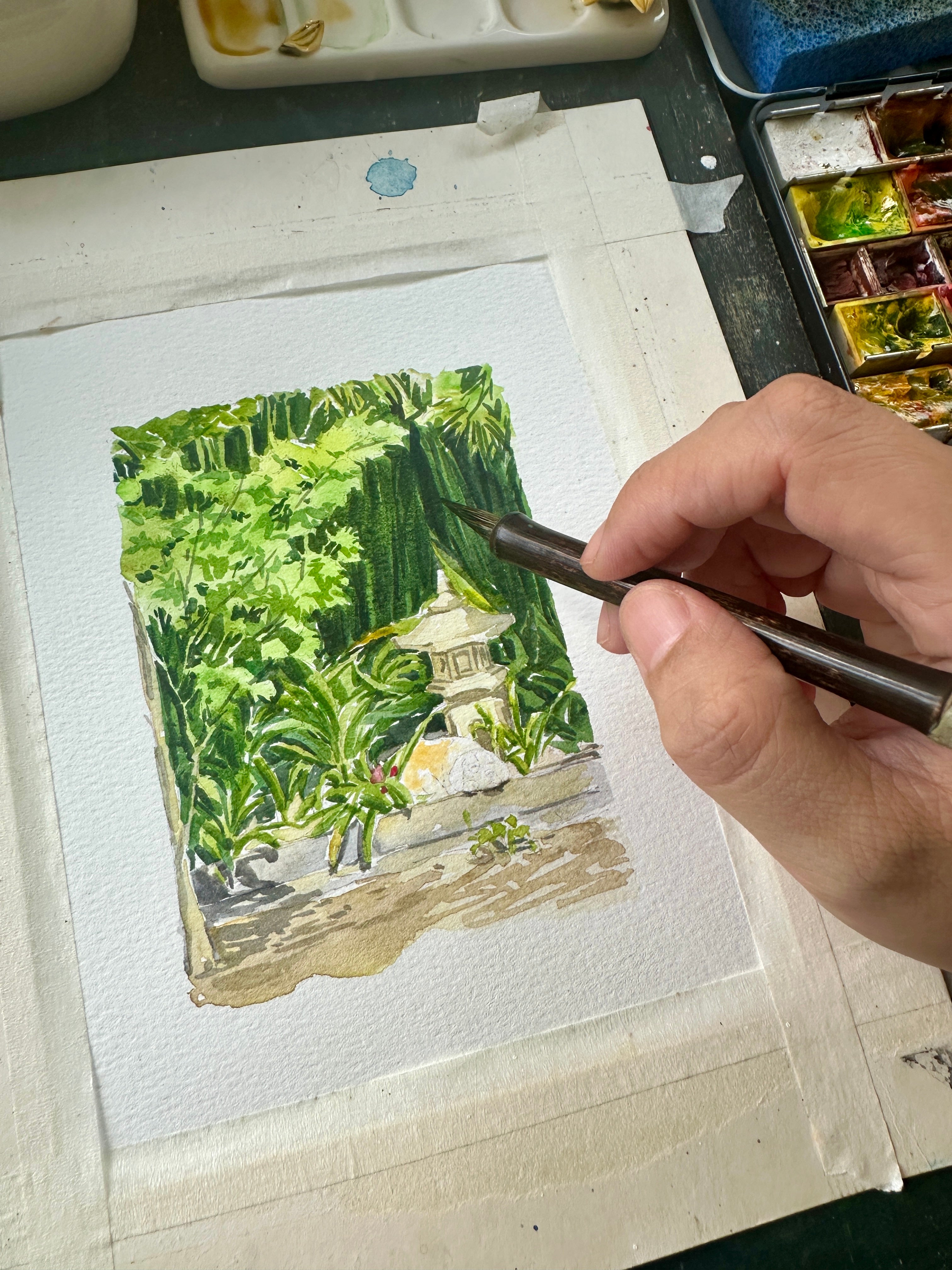 A lush garden landscape watercolor being painted by hand