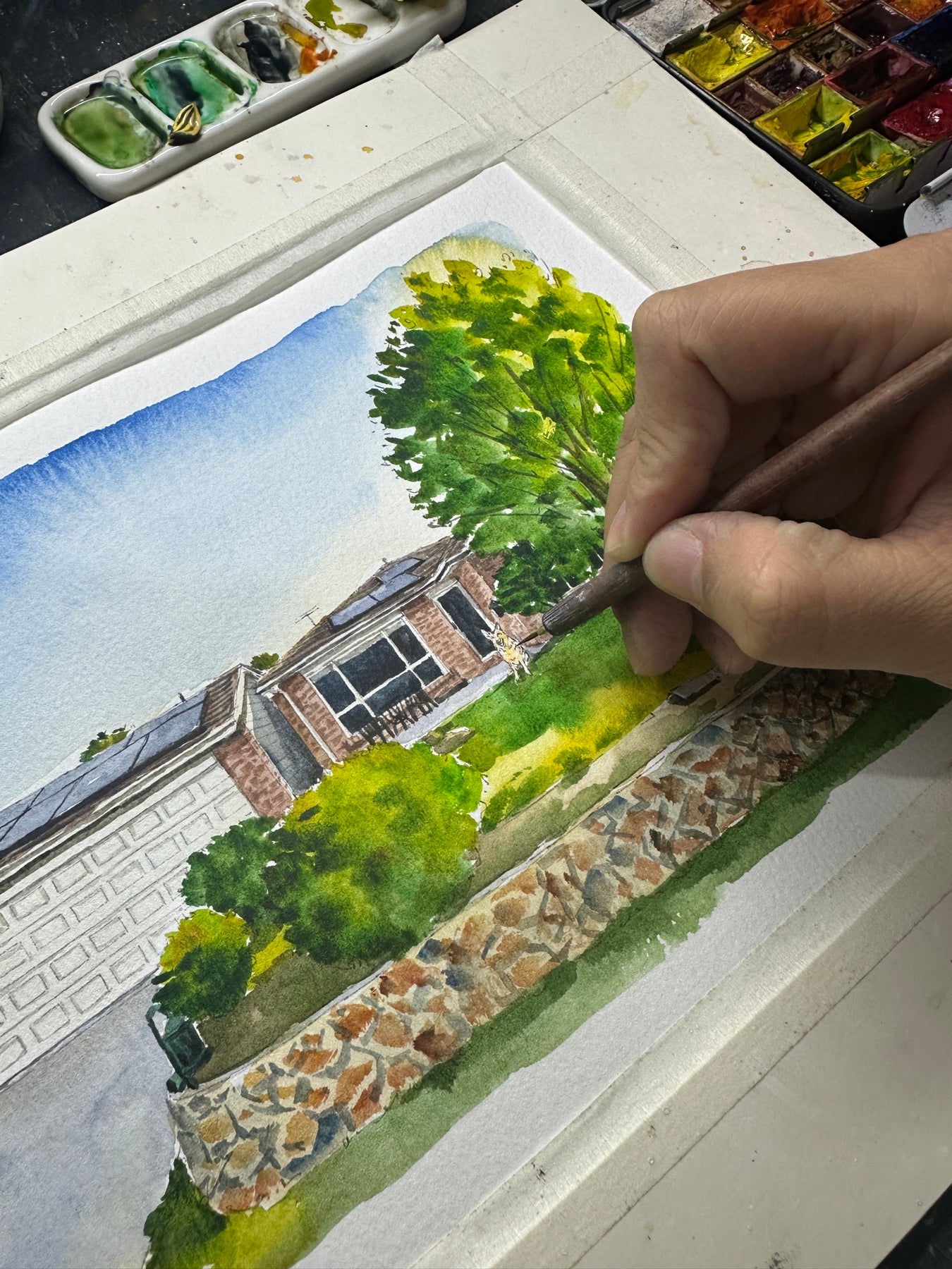 Artist hand-painting a watercolor portrait of a home with a stone garden wall